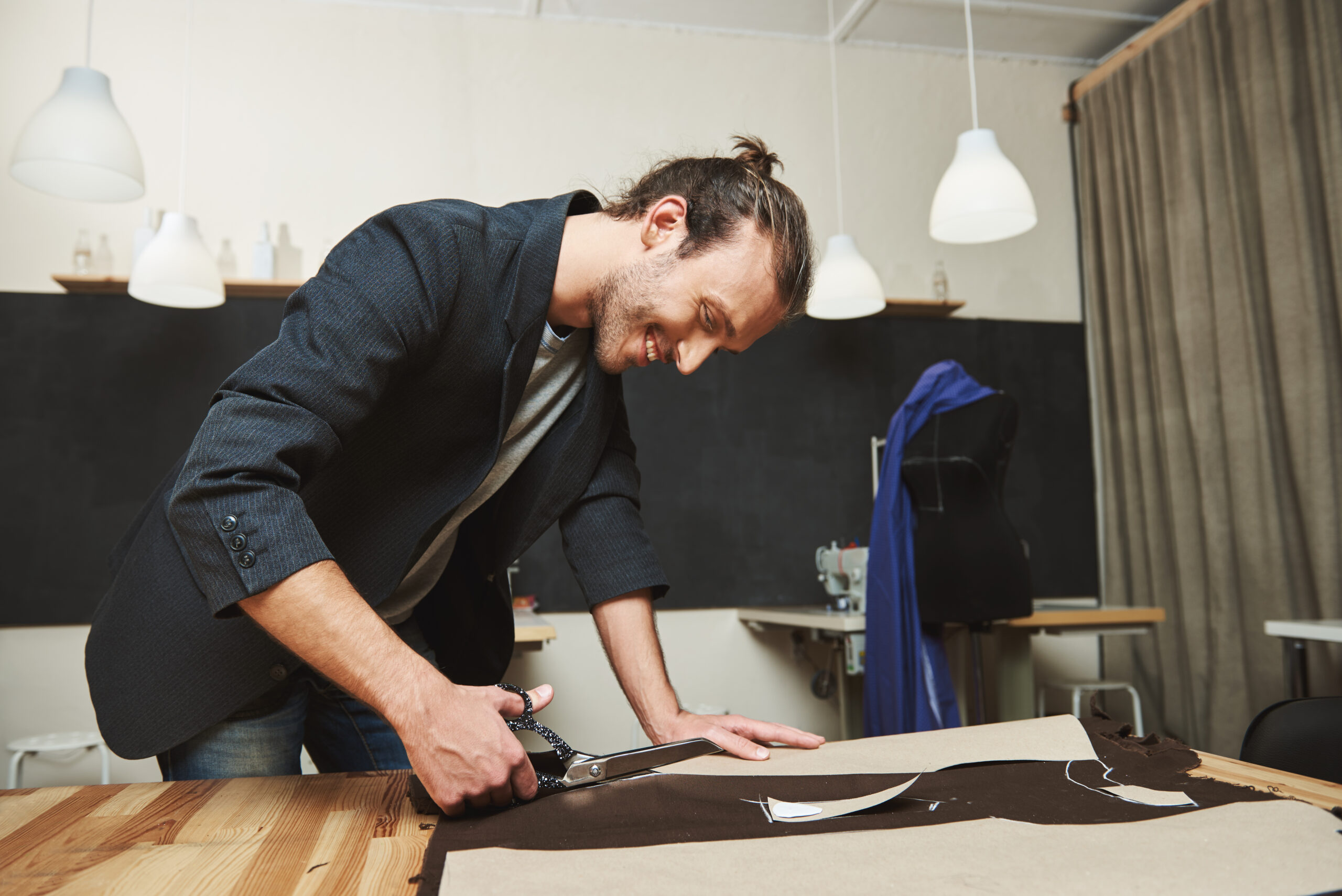 Mature joyful attractive dark-haired hispanic, male fashion designer working on new dress in workshop, cutting out parts, making patterns, sewing parts together